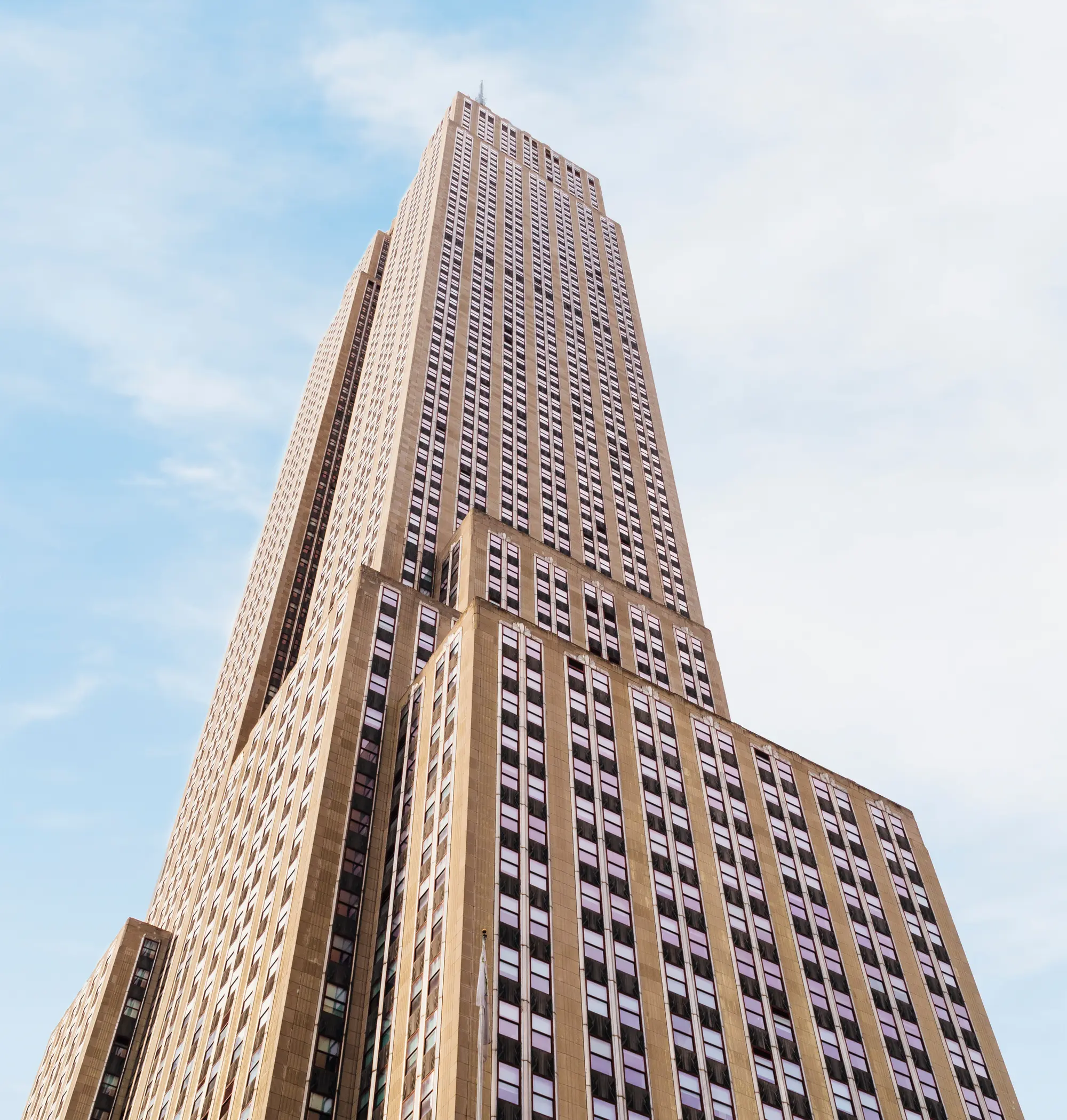 Low-angle view of a tall Art Deco skyscraper with vertical windows rising into a pale blue sky.