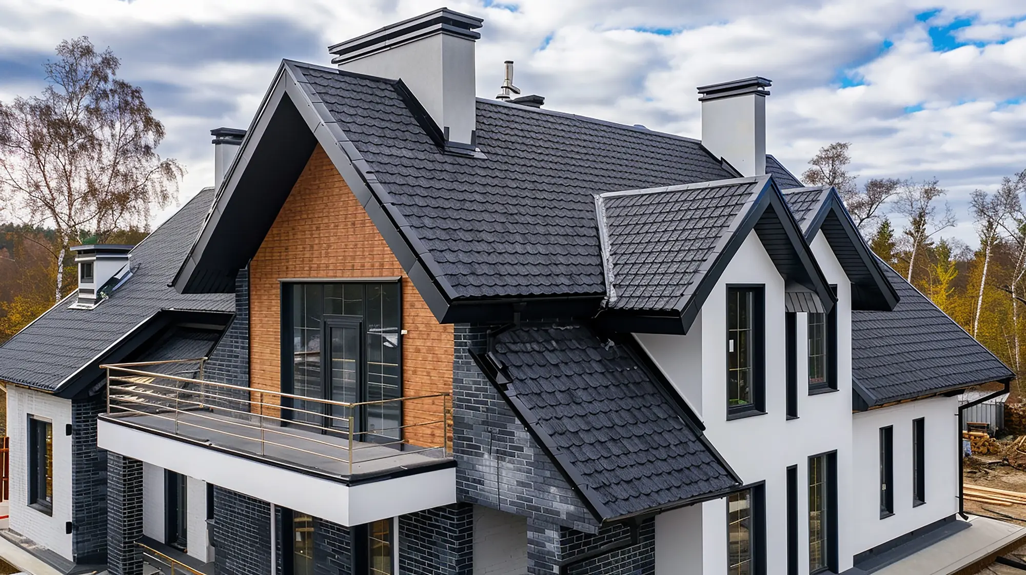 Modern two-story house with dark shingle roof, white and brick exterior, and a balcony railing under a cloudy sky.